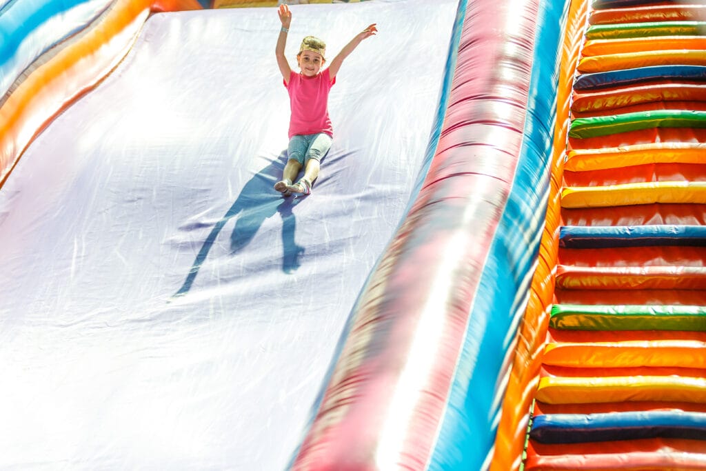 Young girl joyfully sliding down a colorful inflatable slide, capturing a moment of fun and excitement at an outdoor event.