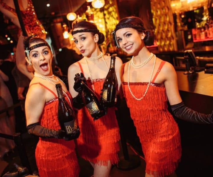 Guests in vibrant costumes and feathered accessories enjoy a Moulin Rouge party Jacksonville FL, with lively music and dancin
