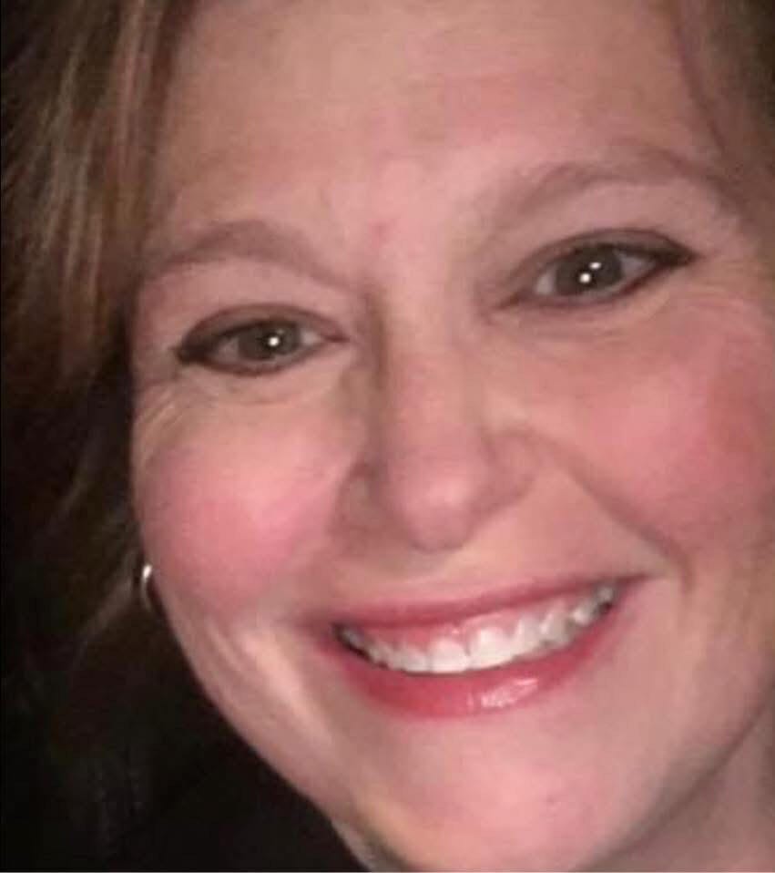 Jacki Culin smiling at a Jacksonville party company event planning session, wearing a professional outfit, with a blurred bac