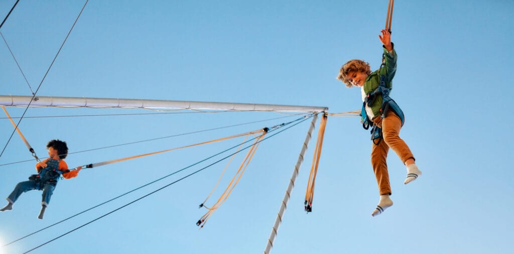 African American girl with afro hair and Caucasian boy jumping on a trampoline with elastic bands at a carnival.