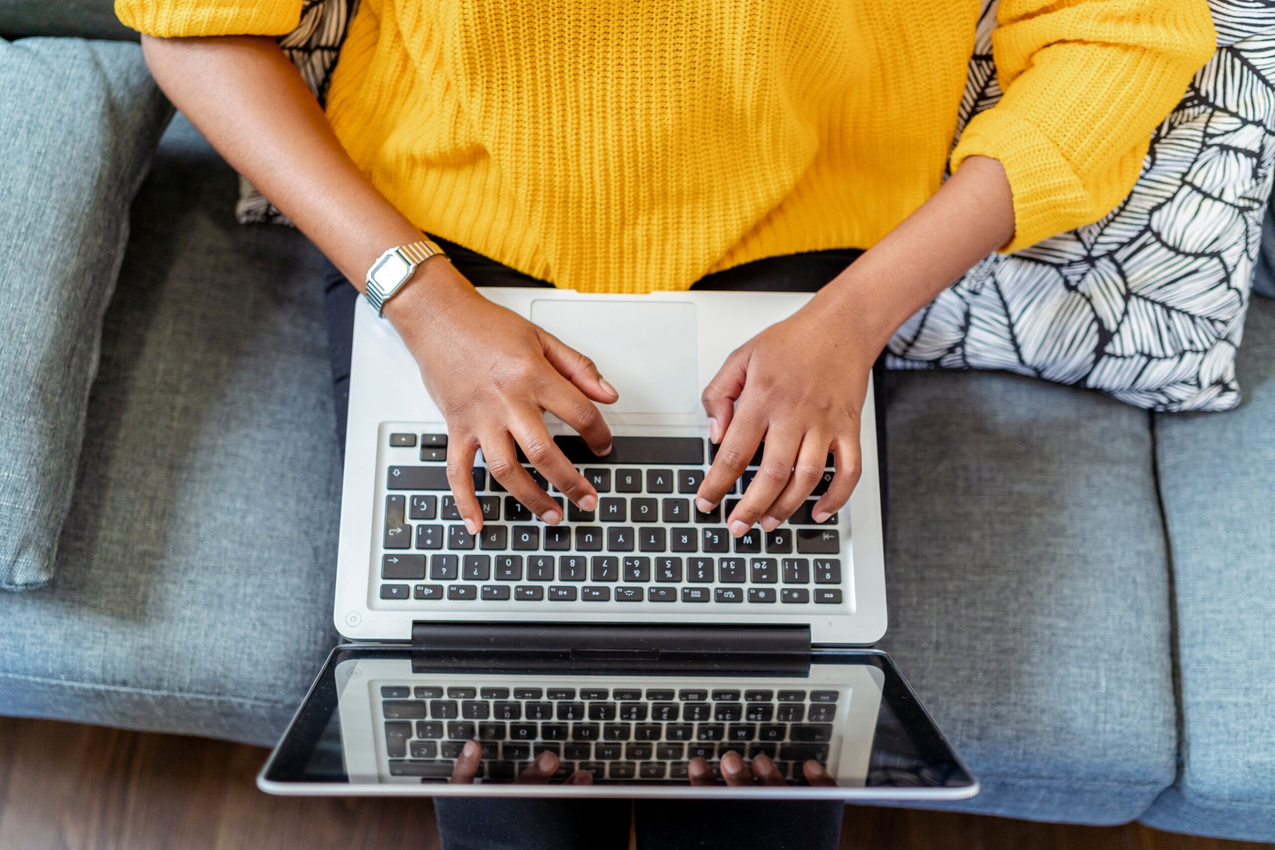 Woman in yellow sweater sits on couch working from home, related to event planning Jacksonville FL.