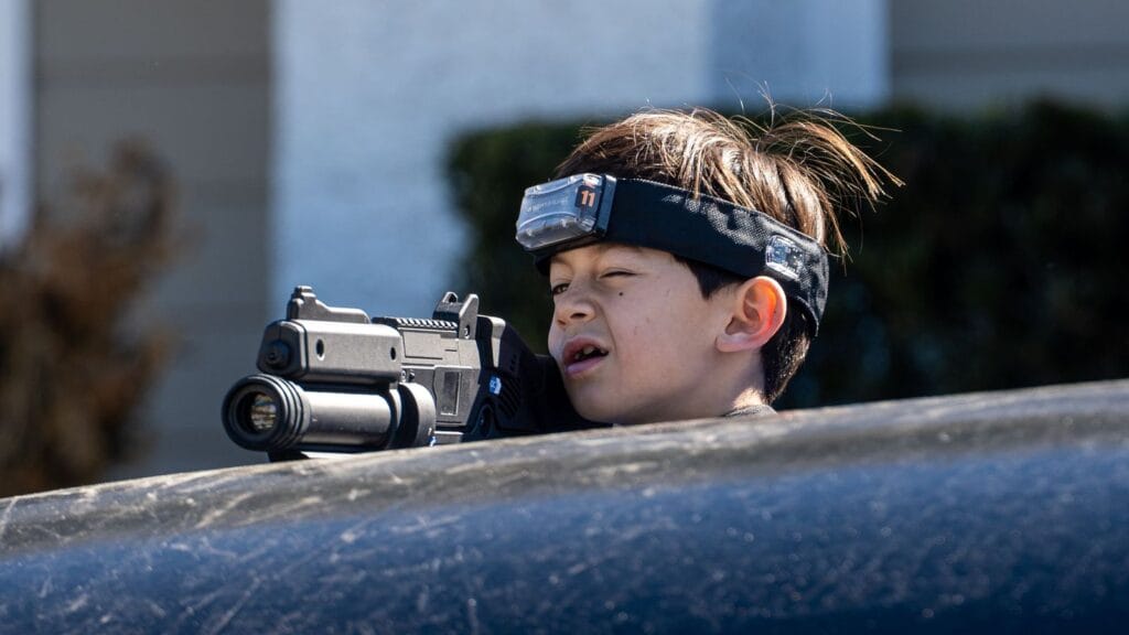 A group of people playing laser tag in a dimly lit arena, wearing vests and holding laser guns, surrounded by neon lights.