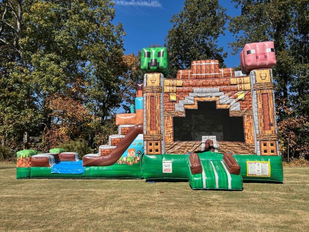 Colorful inflatable bounce house with Minecraft theme, featuring pixelated blocks and characters, set up on grass.