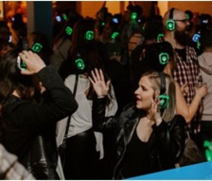 Young people dancing with headphones at a vibrant silent disco, enjoying music and colorful lights.
